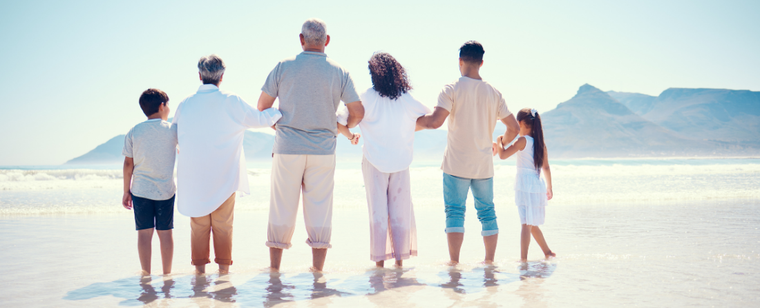 A multigenerational family standing arm in arm looking out at the sea
